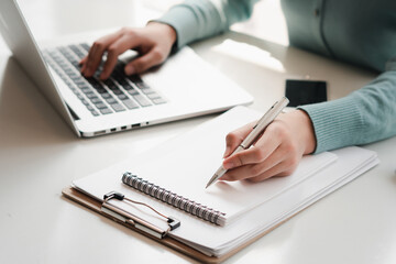 Business women work on computers and write on notepad with pen to calculate financial statements within the office.