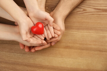 Top view of parents and kid holding red heart in hands at wooden table, space for text. Family day
