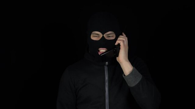 A man in a balaclava mask is talking on a phone fr