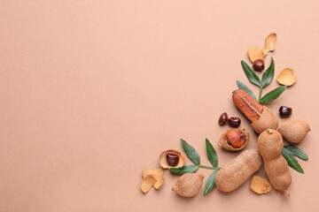 Ripe tamarinds and fresh leaves on beige background, flat lay. Space for text