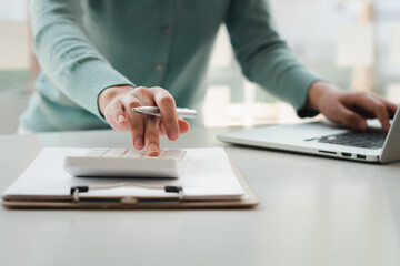 businessman or accountant hand working on calculator to calculate business data, accounting document and laptop computer at office, business concept