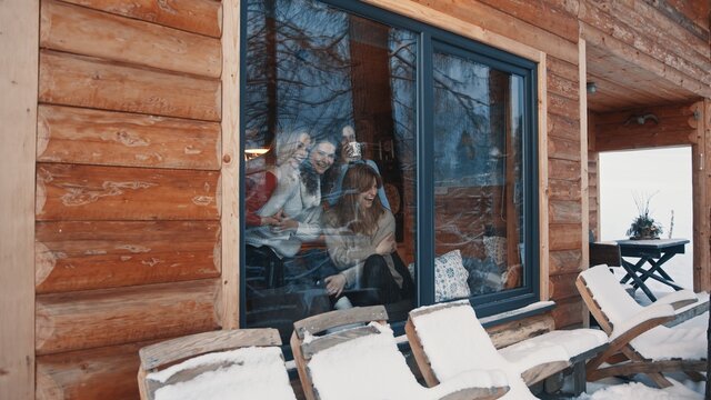 Women, best friends spending winter vacation in wooden mountain house. Drinking hot beverages and gossiping near the big window. High quality photo