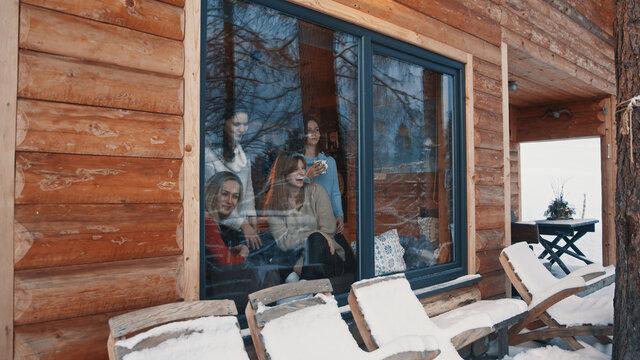 Young women celebrating new year in mountain hut. Drinking hot beverage and looking through the window. High quality photo