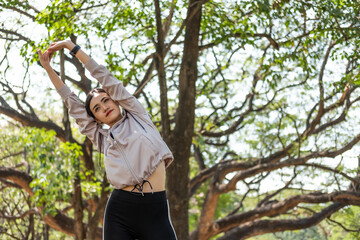 Naklejka na ściany i meble Young beautiful Asian women using smart watch to track activity and listen music from smartphone while warm up and stretch before exercise yoga with natural and trees at background.