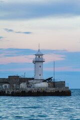 Yalta lighthouse against the backdrop of the rolling sea and evening twilight.