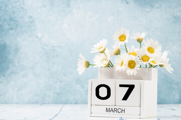 White cube calendar for march decorated with daisy flowers over blue with copy space