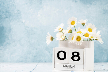 White cube calendar for march decorated with daisy flowers over blue with copy space