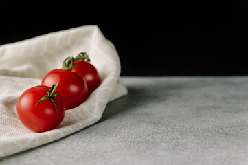 Red tomatoes with green leaves on cloth on gray background
