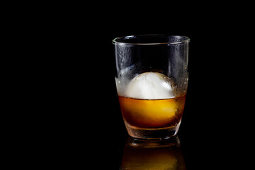 Cold americano decoration with ice ball in whisky glass on a black table.