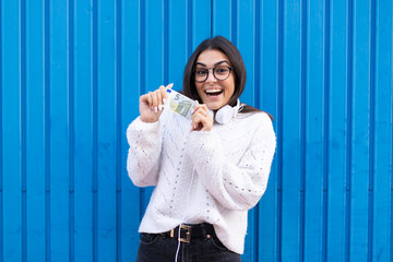 Young brunette woman using headphones amazed with a 5 euro bill in hand