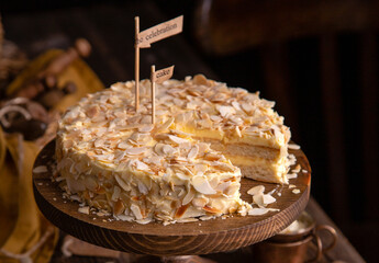 tasty homemade cake with two biscuit layers, white cream and almond flakes on wooden cake stand on rustic table