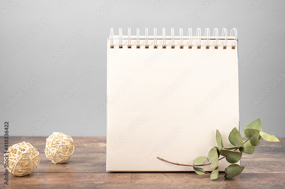 Poster mockup of notebook with blank sheet of paper stands on wooden table on gray background decorated wit
