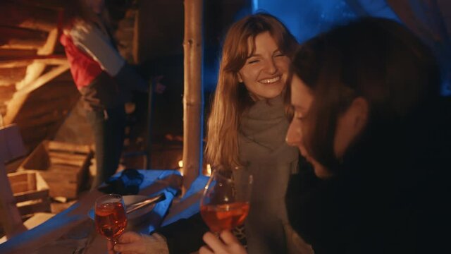 Young women spending winter holidays in cozy mountain wooden cotage drinig mulled wine and gossiping. High quality 4k footage