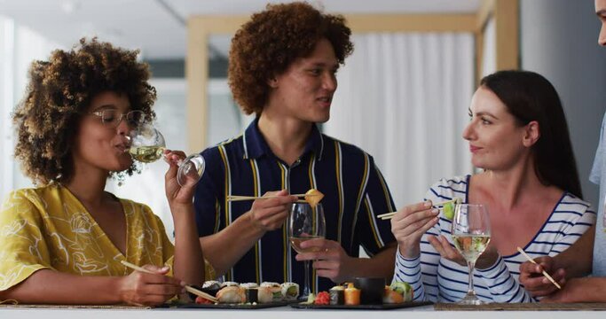 Diverse group of happy friends drinking wine eating sushi and talking at a bar