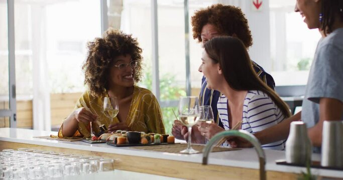 Diverse group of happy friends drinking wine eating sushi and talking at a bar
