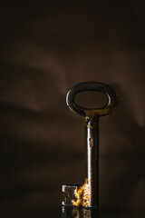 Old, vintage, rusty key in the middle of a frame with front view shot. Close-up picture of a grunge metal key with warm shine behind. Laying on textured abstract light background.