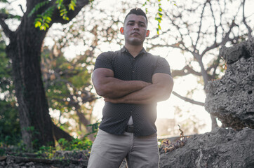 White-skinned male model of Venezuelan origin in the Dominican Republic. sexy man in jeans in the park outdoors with orange walks in natural sunlight among the leaves with his arms crossed