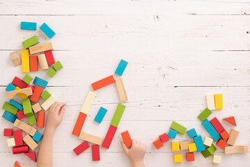 Hands of a child playing with colorful wooden toy blocks and building shapes in the shape of a...