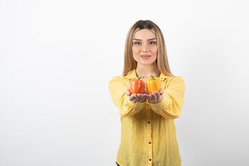 Portrait of positive woman offering colorful bell peppers over white wall