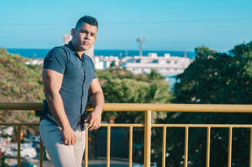 White-skinned male model of Venezuelan origin in the Dominican Republic. sexy man in jeans in the park outdoors with orange walks with natural sunlight among the leaves leaning on a railing