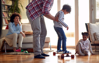 Fototapeta premium A young father helping his son riding the skateboard at home. Family, together, love, playtime
