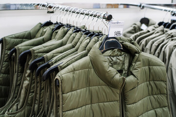 Warm vests made of synthetic materials hang on hangers in the store. Close-up