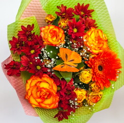 Obraz premium Bouquet of yellow-orange Roses, orange Gerbera and red Chrysanthemums with a plastic butterfly close - up in a package on a white background