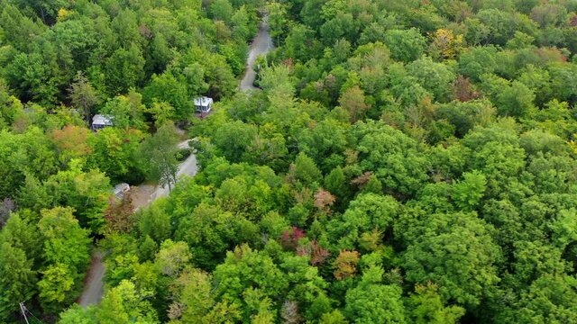 Aerial panning shot of road amidst structures and green trees in forest, drone flying over landscape - Berkshire County, Massachusetts