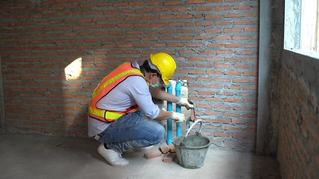 asian bricklayer worker installing brick masonry Closing pvc pipe for water piping system resident in new building