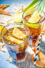 Summer holiday vacation tropical background with iced beverages. Cuba Libre, long island iced tea cocktail with strong alcohol, cola, lime, crushed ice, tropical background with starfish, palm leaves
