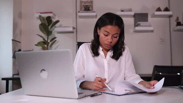 Businesswoman talking in front of laptop and looking at resume at table in company spbi. Young female hr specialist talks in front of computer screen and looks at document while sitting at desk in