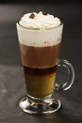 Coffee with cream in a glass mug on a dark background