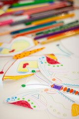 Fototapeta na wymiar Top view of colorful, kid-drawn pictures, felt-tip pens and pencils on a white table. Creative ideas, creativity and early learning. Education concept. Selective focus