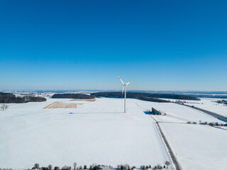 Aerial view of wind turbine in snow covered landscape next to highway A8 near Ulm in Southern Germany on a sunny winter day with great blue sky and shadow visible on the snow