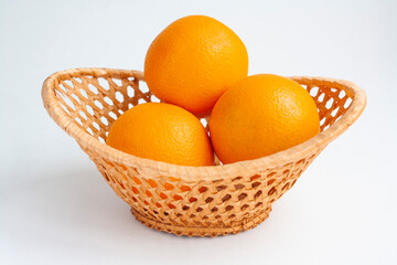 Three ripe oranges in a wicker basket on a white background