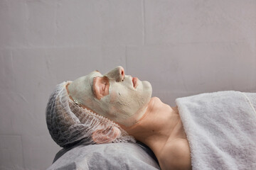 Side view of a young man's face with green natural clay in a beauty salon. Skin cleansing. Natural cosmetics.