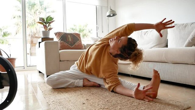 Fit woman sitting on floor and stretching body at home