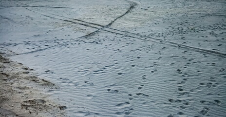 Footprints from people's shoes and motorcycle wheels on the gray sand. Background