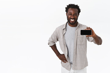 Good-looking african-american bearded man in casual outfit, holding smartphone horizontally and smiling satisfied, giving recommendation what game download, showing his app profile, white background