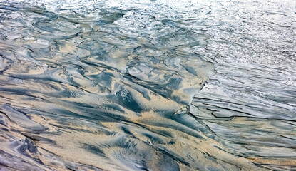 Traces of flowing gray sand with water on the shore of a shallow lake. Background