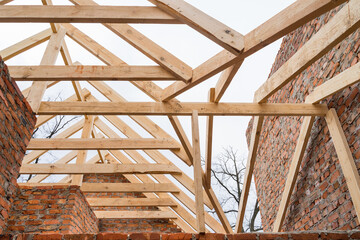 Installation of wooden beams at construction the roof truss system of the brick house.