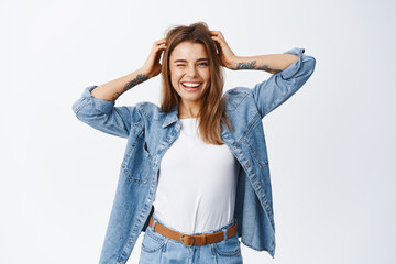 Beauty. Happy young woman touching her hair and winking at camera, smiling excited, showing her...