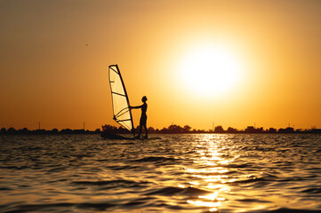 Woman windsurfer silhouette at lake sunset. Beautiful beach landscape. Summer water sports...