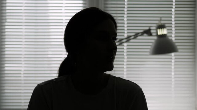 Hidden identity, unknown person, silhouette, interview. Dark female silhouette on background of light from window talking looking at camera