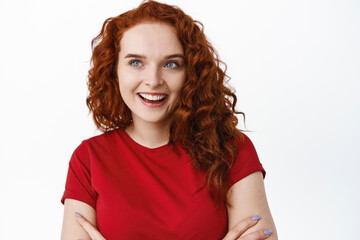 Close-up of silly beautiful girl with ginger curly hair, looking aside at left side logo or advertisement, smiling pleased and determined to buy something, cross arms on chest, white background