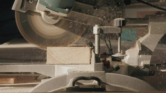 A construction worker cuts a thick board with an electronic saw. Wood shavings are flying around. 4k video.