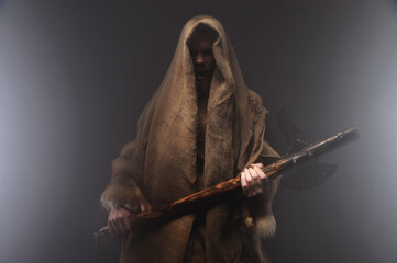 Portrait of a medieval bearded military monk, dressed in animal skins and burlap, holding a battle...
