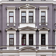 Fototapeta premium Detail of grey purple art nouveau building´s façade of eight windows, white pillars and decorations around the brown windows in Riga, Latvia, Europe where one window has visible pink egg/like figures.