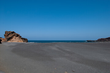 einsamer schwarzer Lavastrand mit dem blauen Ozean im Hintergrund sowie Lavafelsen / Vulkangestein