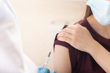 female doctor or nurse giving shot or vaccine injection to a teenager patient. Vaccination and...